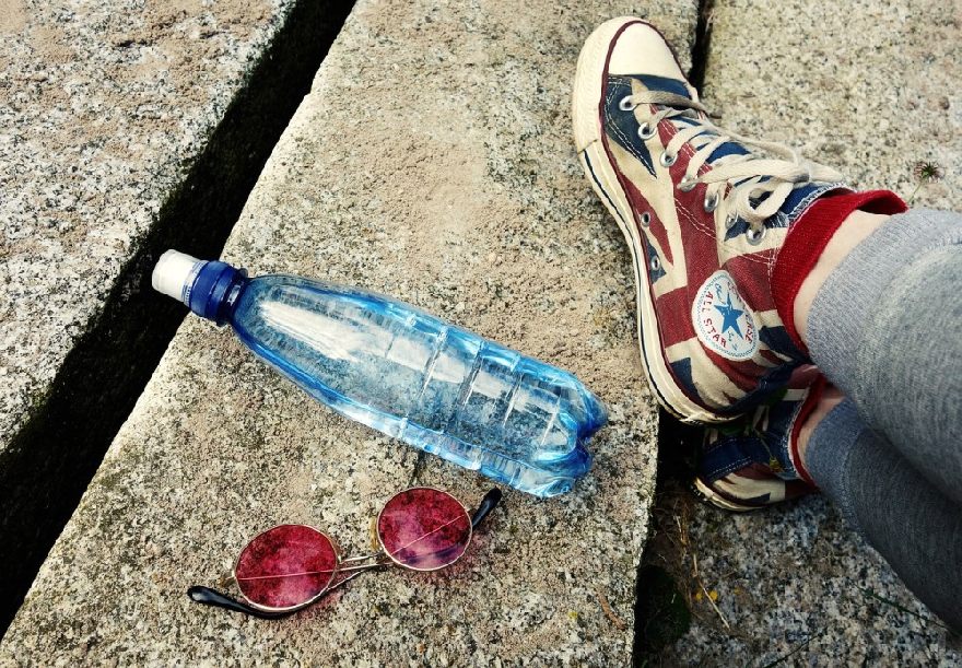 Lunettes de soleil rouges et bouteille d'eau et pieds sur le sol